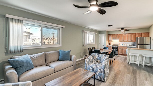 A modern living room with a sofa, a patterned armchair, a wooden coffee table, and a dining area with a table and chairs. - 2 Blocks to Beach & Boardwalk: Ocean City Condo (Ocean City)