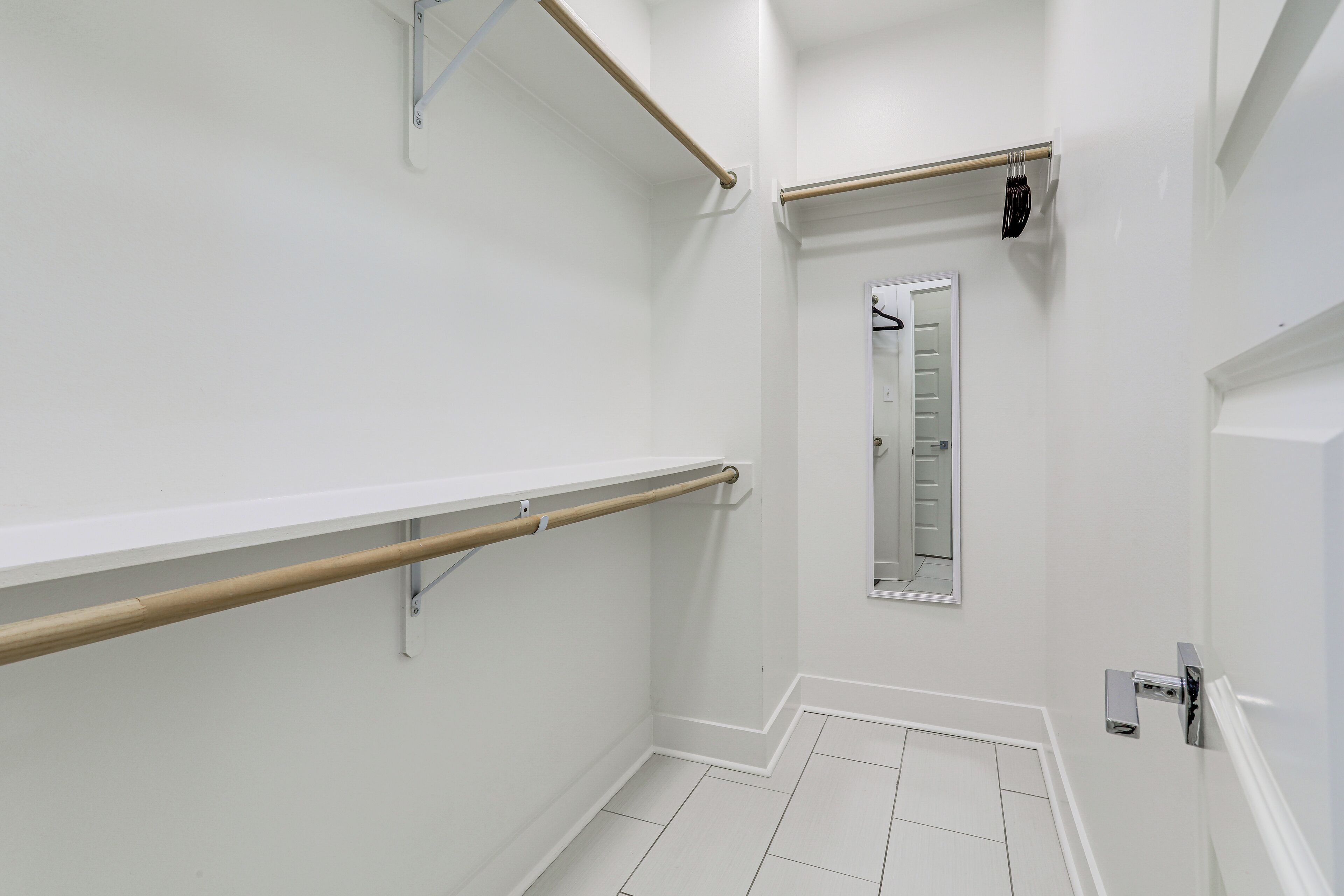 A bathroom with white walls, a wooden handrail, a mirror, and a white door.