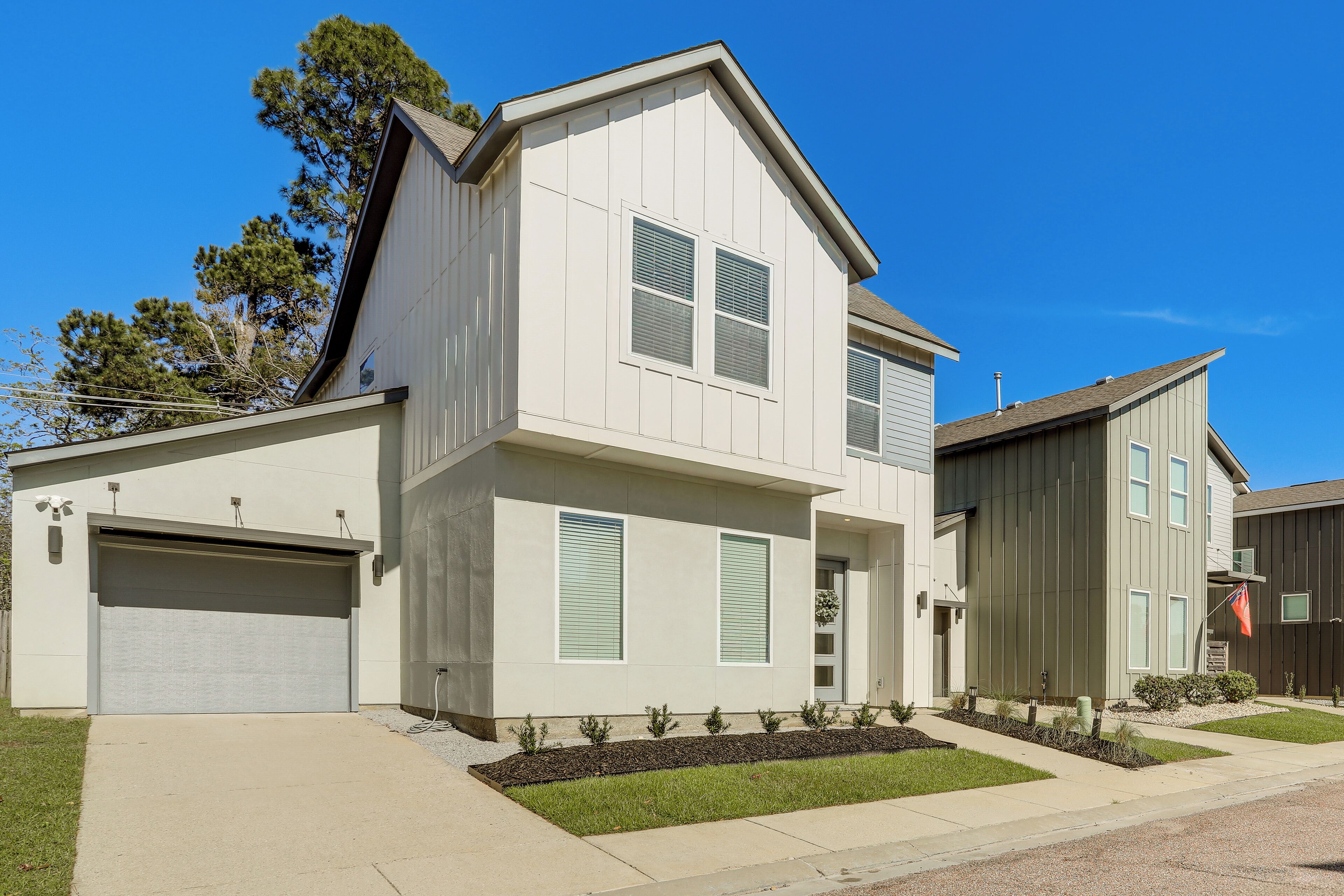 A two-story residential building with a garage, a front porch, and a small garden area.