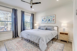 A bedroom with a bed, a nightstand, a lamp, a ceiling fan, and a window with curtains. - Modern 3BR Retreat - Near Bluebonnet & Hospitals (Baton Rouge)