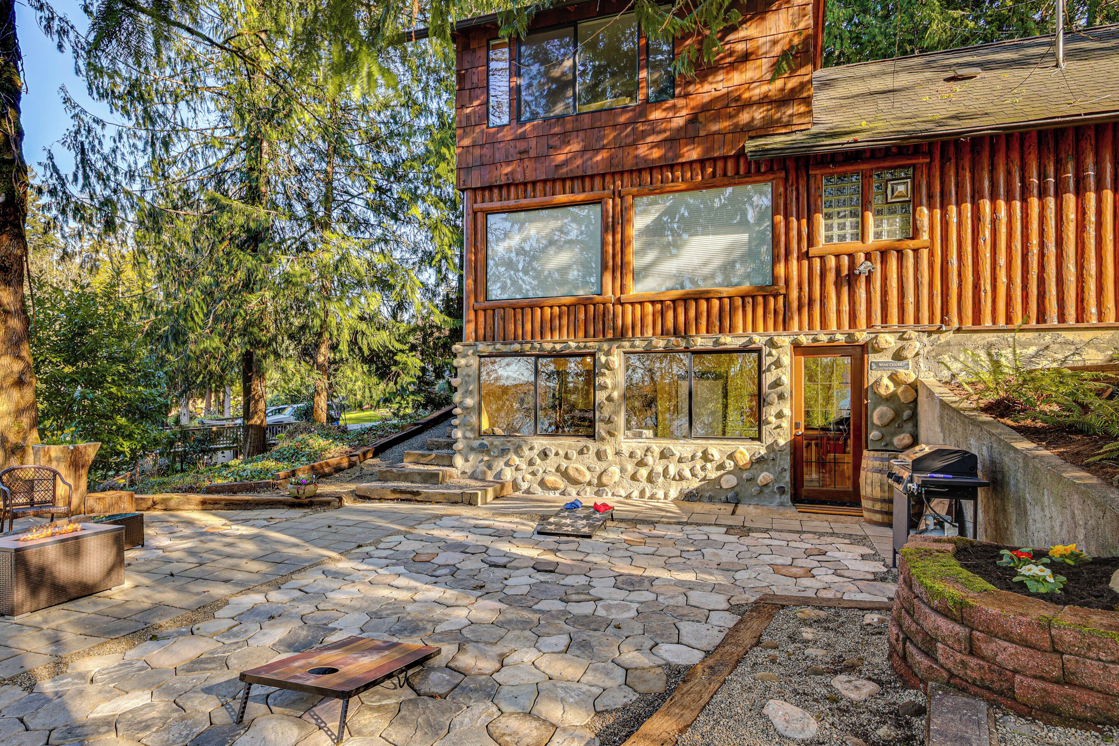 A log cabin with a stone foundation, large windows, and a stone fire pit area.