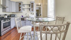 Una cocina con estufa a gas, microondas y armarios. Hay una mesa de comedor con sillas y una lámpara de araña.