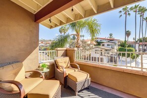 Un balcone con mobili in vimini, un tavolino con una pianta e vista su palme e edifici.