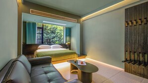 A modern hotel room with a bed, a sofa, a coffee table, and a view of greenery outside. - Yangshuo B&G Hotel (Guilin)