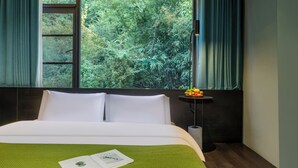 A hotel room with a large window, a bed with white linens, a green throw blanket, and a small table with fruits. - Yangshuo B&G Hotel (Guilin)