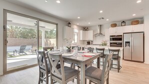 A modern kitchen with white cabinets, a stainless steel refrigerator, and a dining area with grey chairs and a table set for four. - 4 Mi to Empire Polo Club: Getaway w/ Outdoor Oasis (Coachella)