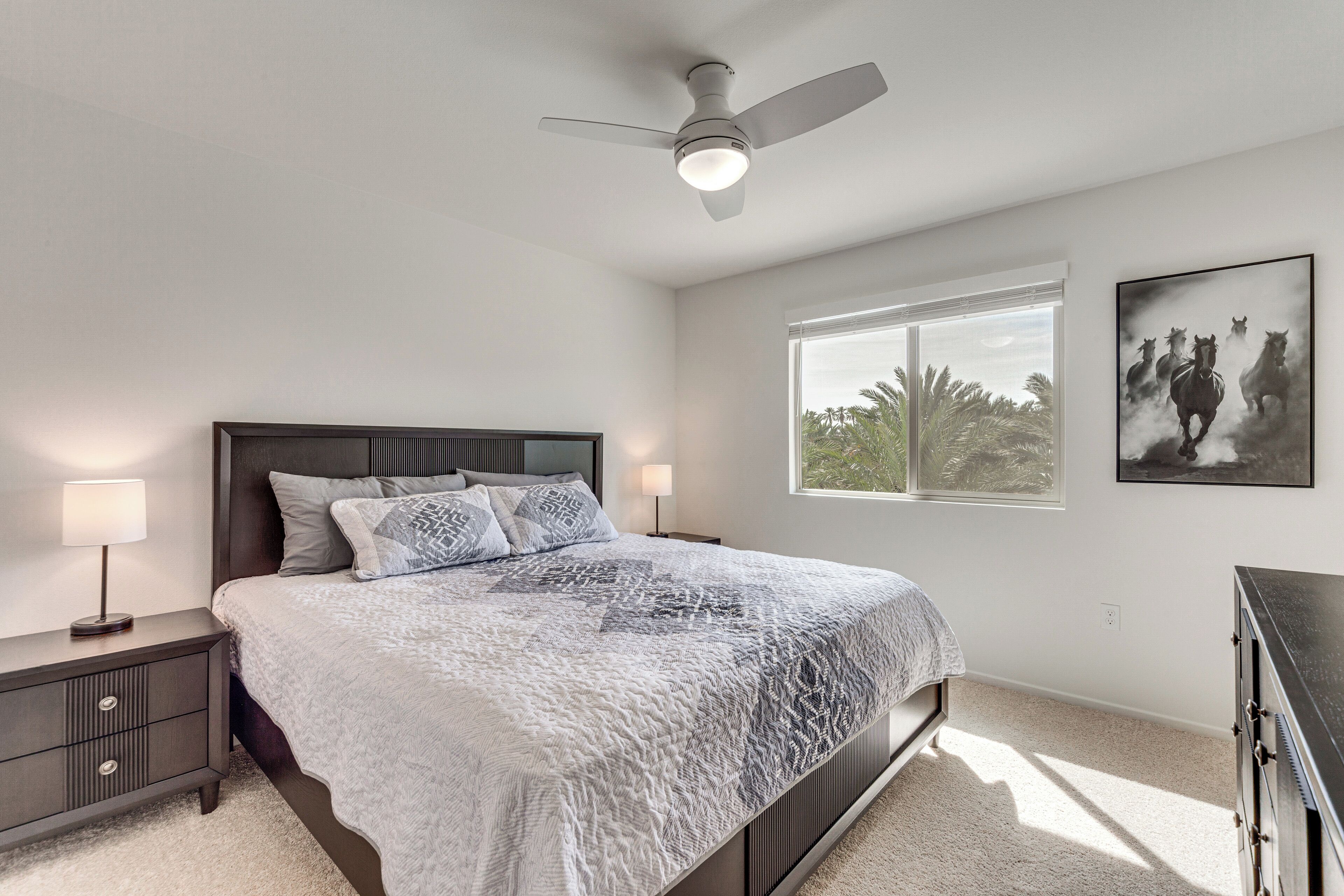A bedroom with a bed, nightstands, a ceiling fan, a window, and a painting.