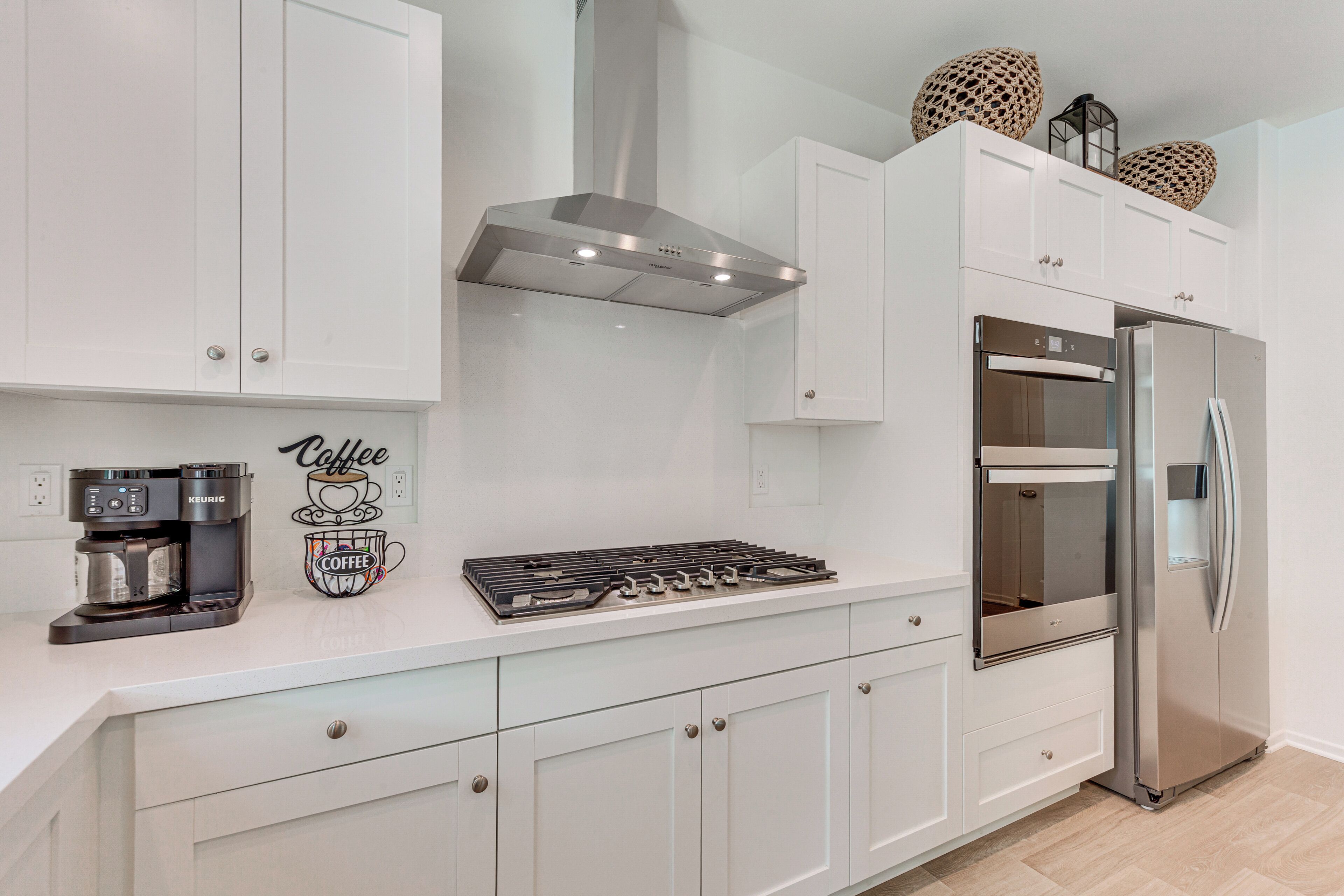 A modern kitchen with white cabinetry, a stainless steel range, a built-in oven, and a coffee maker.