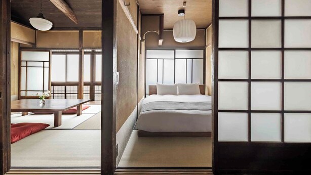 Ein traditioneller japanischer Raum mit Tatami-Boden, einem niedrigen Bett, einer Schiebetür und einer hängenden Leuchte.