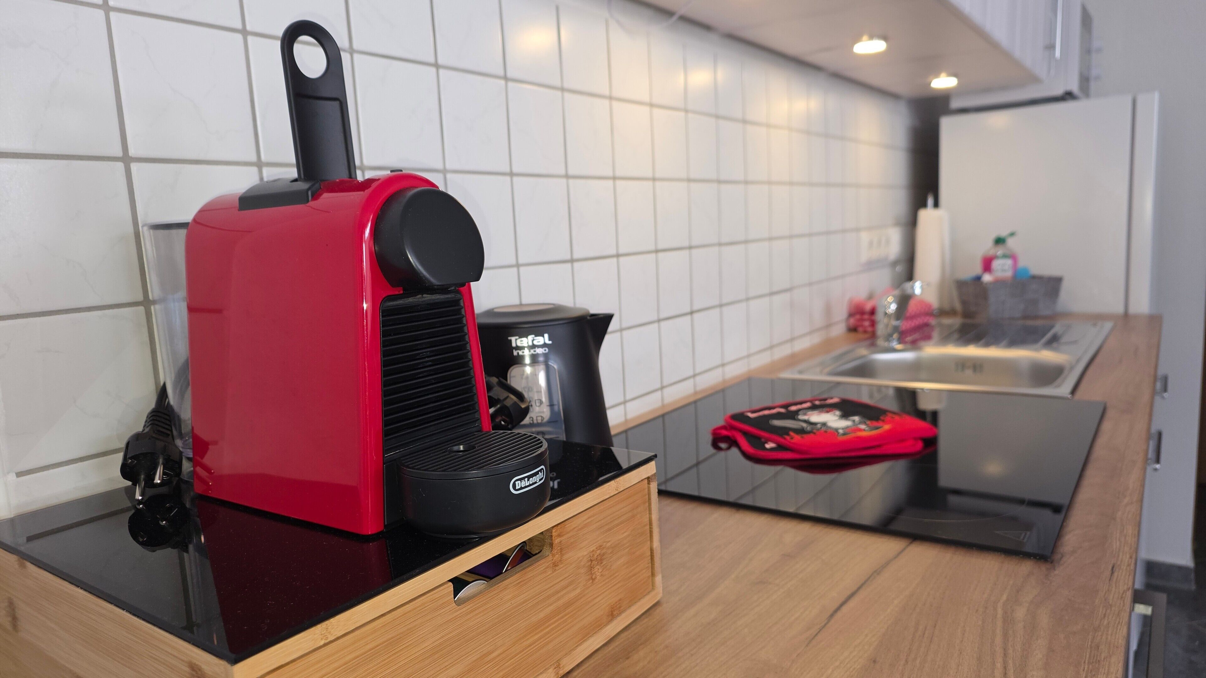 Een keuken met een rode koffiezetapparaat, een zwarte koffiekan en een lade met een zwart voorwerp.