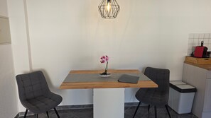 A modern kitchen with a wooden table, two grey chairs, a small orchid plant, and a hanging light fixture.