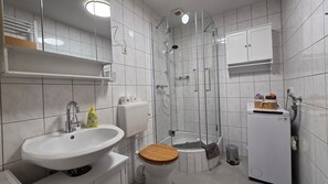 A bathroom with a sink, toilet, shower, and a small white cabinet.