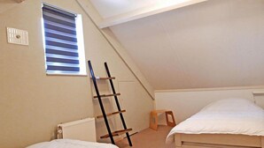 Une petite chambre mansardée, composée d’une seule pièce, avec un plafond en pente, une échelle, un radiateur et deux lits.