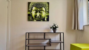 Quarto com pintura de Buda, prateleira de metal preto, planta em vaso e cadeira verde vibrante.