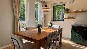 Uma sala de jantar com mesa de madeira, quatro cadeiras, um vaso com flores e uma luminária pendente.