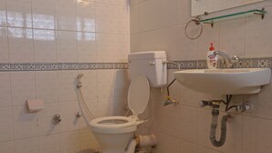 Un baño con inodoro, lavamanos y estante de vidrio sobre el lavamanos.