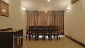 Habitación con ventilador de techo, aire acondicionado, una mesa de comedor con sillas, un cuadro enmarcado y cortinas.