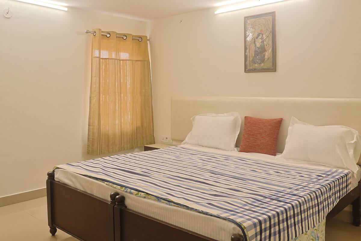 A bedroom with a bed, a nightstand, a curtain, and a wall-mounted picture.