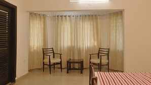 Una habitación con cama, dos sillas, una mesita y un ventanal con cortinas.
