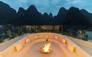 A fire pit surrounded by seating, with a mountainous landscape in the background. - Yangshuo Minos Hotel (Guilin)