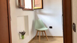 Un couloir doté d’un plancher en bois, d’une chaise verte, d’une plante en pot et d’un climatiseur fixé au mur.