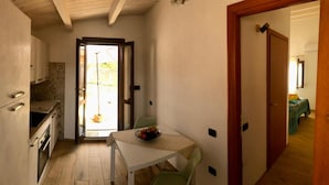 Une cuisine compacte avec un coin repas, une petite table sur laquelle on voit des fruits, et une vue à travers une porte ouverte.