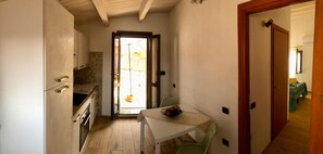 Una cucina compatta con zona pranzo, un tavolino con della frutta e vista attraverso una porta aperta.