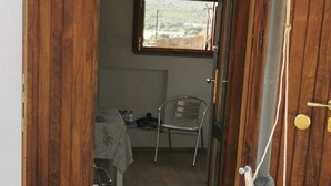 Une porte en bois qui donne sur une pièce avec une fenêtre, une chaise et une plante en pot.