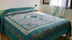 Une chambre à coucher avec un lit, un tableau représentant un coucher de soleil, une fenêtre avec des rideaux et un ventilateur de plafond.