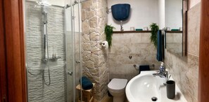 Ein Badezimmer mit Duschkabine aus Glas, einer weißen Toilette, einem Waschbecken mit Spiegel und einem blauen Handtuch auf einem Hocker.