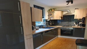 A modern kitchen with a stainless steel refrigerator, a sink, a stove, and wooden cabinets. - Forest Bungalow w/ Sauna for 6 (Ewijk)