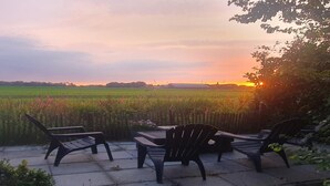 An outdoor seating area with chairs and a table, overlooking a field and a sunset. - Forest Bungalow w/ Sauna for 6 (Ewijk)