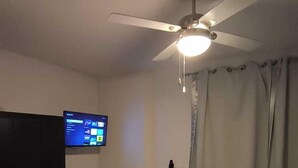 Ein Schlafzimmer mit Bett, Deckenventilator, Fernseher an der Wand und einem dunkelbraunen Kleiderschrank.
