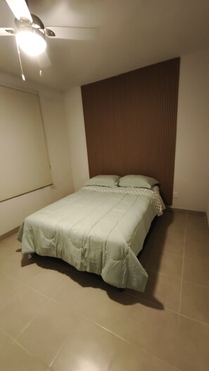 A single bed with a green bedspread, a ceiling fan, and a wooden panel wall.