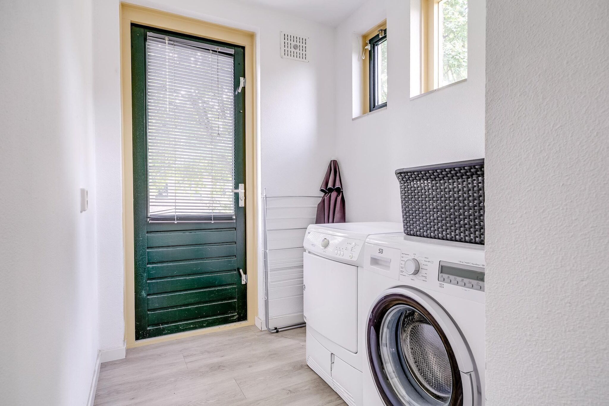 Un cuarto de lavandería con lavadora, secadora y una puerta verde con persianas.