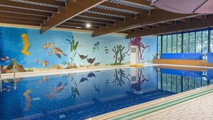 Una piscina interior con un mural de vida marina, un banco de madera y suelo de baldosas.