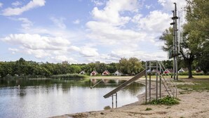 Zona junto al lago con un tobogán de metal, una escalera y un poste de servicios.