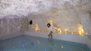 A person in a white robe sitting on the edge of an indoor pool with a textured ceiling and candles. - Cotton Castle Hotel - Yangshuo Eternal (Guilin)