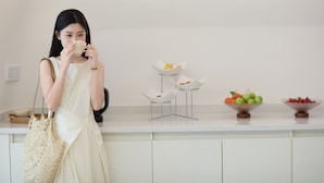 A woman in a white dress holding a cup, standing in front of a buffet with bowls of fruit and a white counter. - Cotton Castle Hotel - Yangshuo Eternal (Guilin)
