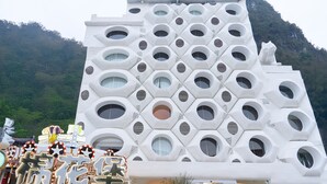 A modern building with a unique geometric facade, a sign reading 'RAMUKKALE,' and a mountain backdrop. - Cotton Castle Hotel - Yangshuo Eternal (Guilin)