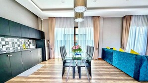A modern kitchen with dark cabinets, a dining table with chairs, and a blue sofa. - For You Breeze Casa Private Pool Villa with 3 bedrooms, Near Cha-Am Beach (Khao Yai)