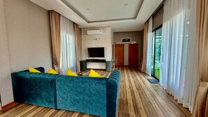 A modern living room with a sofa, TV, and wooden flooring. - For You Breeze Casa Private Pool Villa with 3 bedrooms, Near Cha-Am Beach (Khao Yai)
