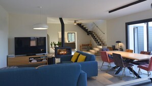 A modern living room with a flat-screen TV, a fireplace, a sofa, and a dining area with chairs. - Gorgeous Mansion for 6 in Barjac (Barjac)