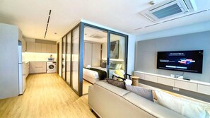 A modern hotel room with a kitchenette, a sofa, a TV, and a sliding door leading to a bathroom. - Luxurious One bedroom Condo with Pool View at The Aqua Boat Avenue near Laguna (Tambon Choeng Thale)