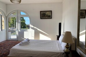 Ein Hotelzimmer mit Bett, Lampe, Gemälde und Blick durch ein Fenster.