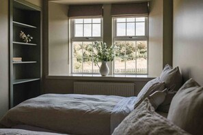 Ein Schlafzimmer mit Bett, Fenster mit Ausblick, Heizkörper und Bücherregal.