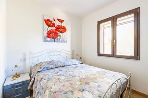 A bedroom with a bed, a nightstand, a painting, and a window. - Apartment with air conditioning (Tergu)