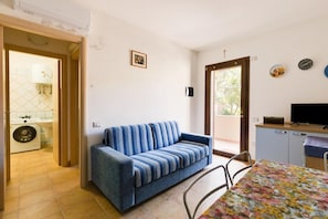 A room with a sofa, a table with a floral tablecloth, a television on a cabinet, and a door leading to a balcony. - Apartment with air conditioning (Tergu)