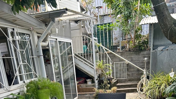 Un espace extérieur aménagé avec des meubles en osier et une table en verre, entouré de plantes en pot et agrémenté d’un escalier menant à un niveau supérieur.