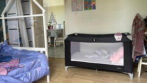 Une pièce avec un lit superposé, un berceau, un calendrier mural et une petite table avec des chaises.